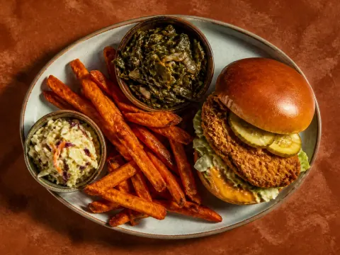 Representative a crispy halal chicken sandwich with sweet-potato fries, collard greens, and a small slaw selected for Busboys and Poets