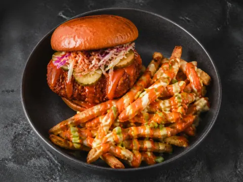 Representative a halal Nashville-style hot chicken sandwich with slaw, pickles, spicy glaze, and loaded fries selected for CHAR'D (Pike & Rose)
