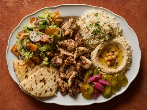 Representative a Levantine grilled chicken shawarma plate with hummus, fattoush, pickles, rice, and pita selected for Haifa Grill