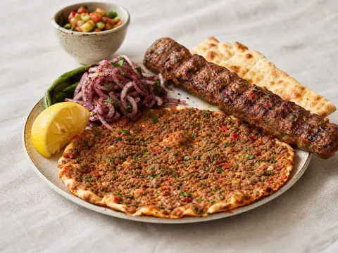 Representative Turkish lahmacun with minced halal beef and herbs beside adana kebab, sumac onions, and lemon selected for Ottoman Kitchen