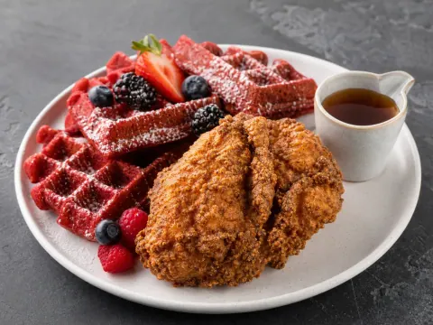 Representative halal fried chicken breast with red velvet waffles, berries, powdered sugar, and a small maple syrup pitcher selected for Southern Style Chicken & Waffle (District Heights)